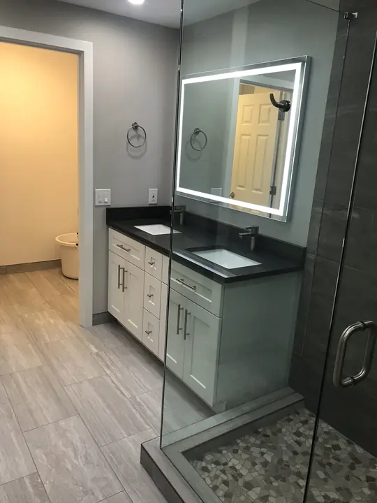 Double vanity with LED mirror beside a pebble-floor glass shower