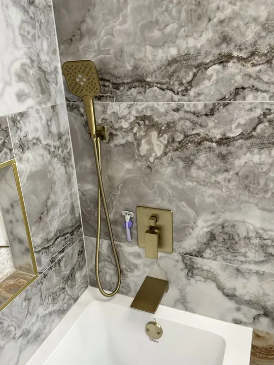 Brushed-gold tub fixtures against veined marble tile