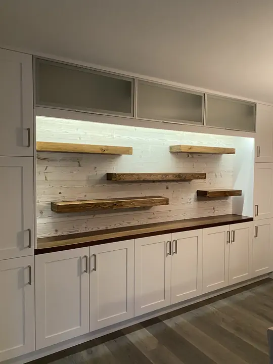 Built-in cabinetry with lit wall and reclaimed-wood floating shelves