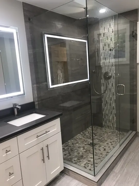 Charcoal tile shower beside a double vanity with LED mirror