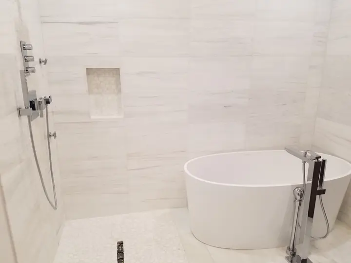 Freestanding soaking tub beside an open marble shower
