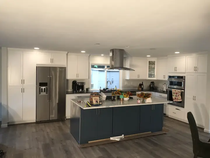 Open white kitchen with a navy island and stainless hood