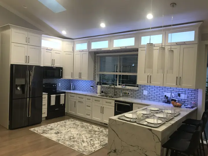 White shaker kitchen with marble-look island and lit transom cabinets