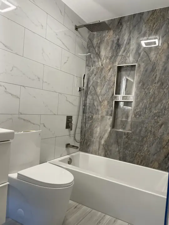 Tub and shower with dramatic stone feature wall and lit niche